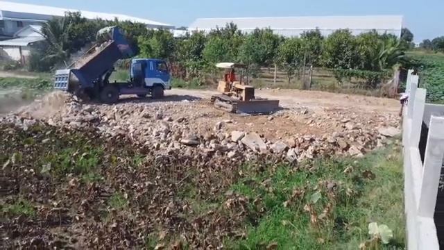 бульдозер толкает дробильные отходы, расчищая строительный камень самосвалами